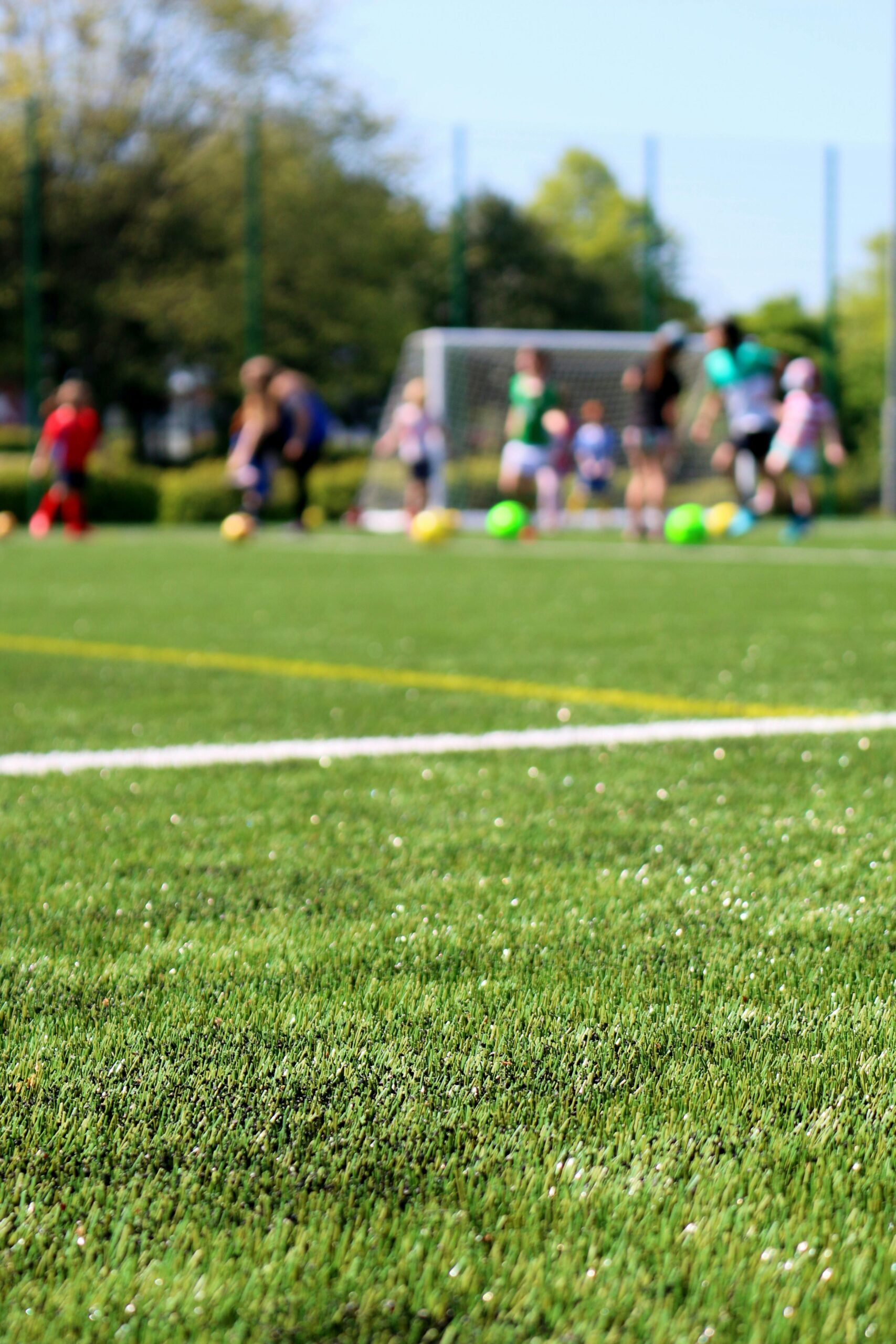 Blurred children playing soccer on a vibrant green field during a sunny day.