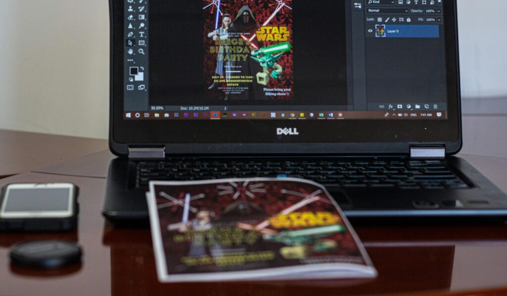 A laptop displaying Star Wars party invitation design in a workspace setting.