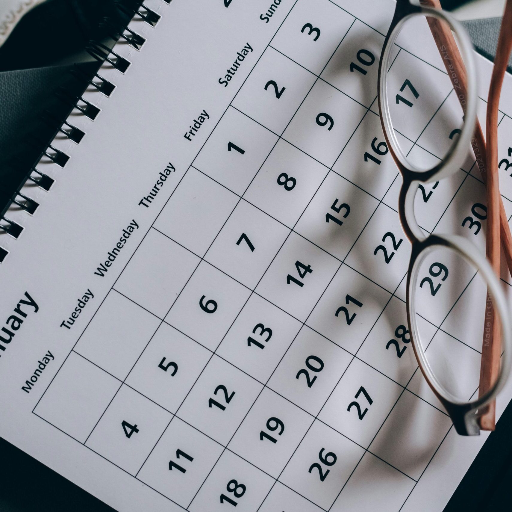 A close-up of a January calendar with eyeglasses on a table, emphasizing planning and organization.